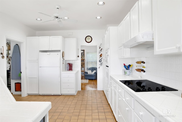 kitchen featuring tile counters, freestanding refrigerator, white cabinetry, under cabinet range hood, and black electric cooktop