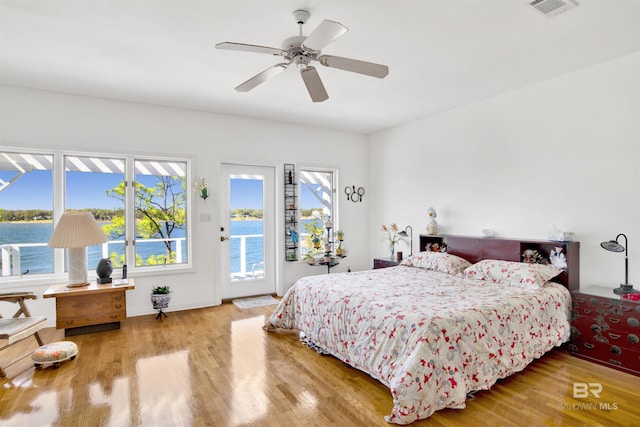 bedroom featuring a water view, access to outside, visible vents, and wood finished floors