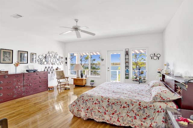 bedroom with access to outside, wood finished floors, visible vents, and a ceiling fan