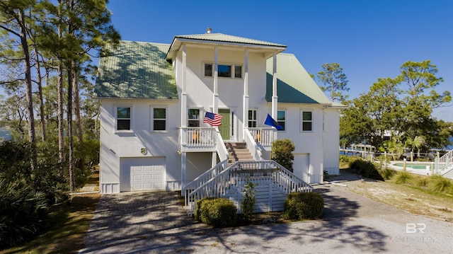 raised beach house with metal roof, a porch, an attached garage, stairway, and stucco siding