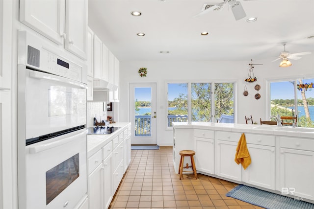 kitchen with tile countertops, double oven, black electric cooktop, white cabinets, and backsplash