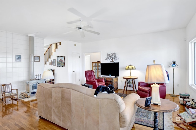 living area featuring ceiling fan, stairs, wood finished floors, and a wood stove