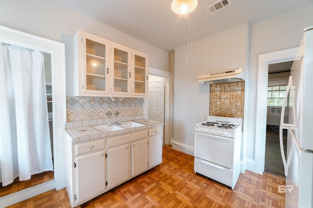 kitchen with white appliances, sink, backsplash, white cabinetry, and tile counters