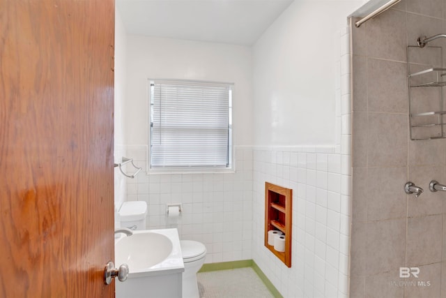 bathroom featuring vanity, toilet, tiled shower, and tile walls