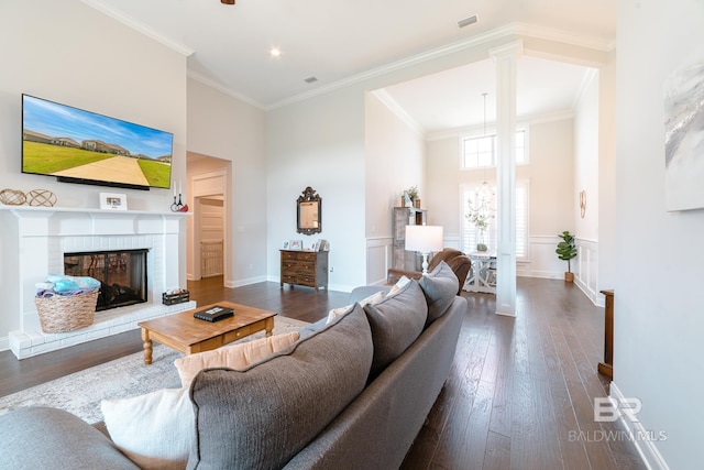 living room with a brick fireplace, ornamental molding, dark wood-type flooring, and decorative columns