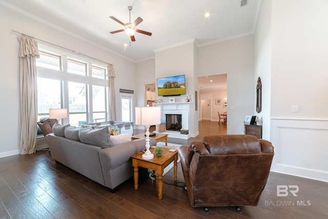 living room with ceiling fan, a high ceiling, dark hardwood / wood-style floors, and ornamental molding