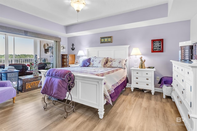 bedroom featuring baseboards, light wood-style floors, a raised ceiling, and access to exterior