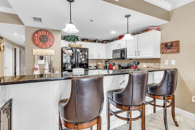 kitchen with visible vents, black appliances, a kitchen bar, tasteful backsplash, and white cabinetry