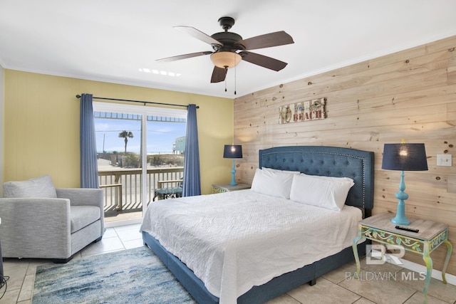 bedroom with ceiling fan, light tile patterned floors, wood walls, and access to exterior