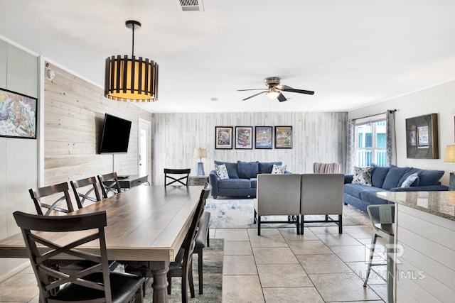 dining room featuring ceiling fan, light tile patterned flooring, and wood walls