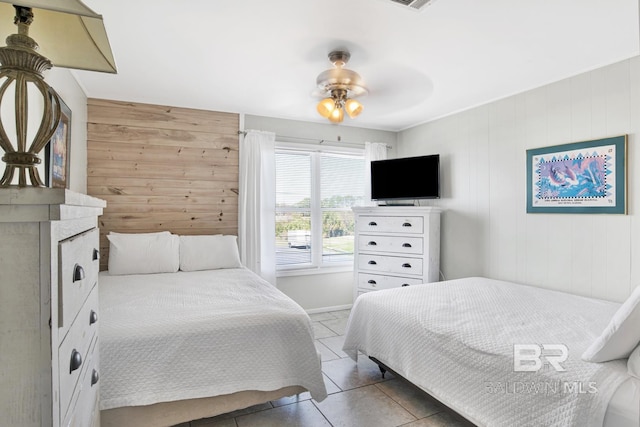 bedroom with ceiling fan, wood walls, and tile patterned floors