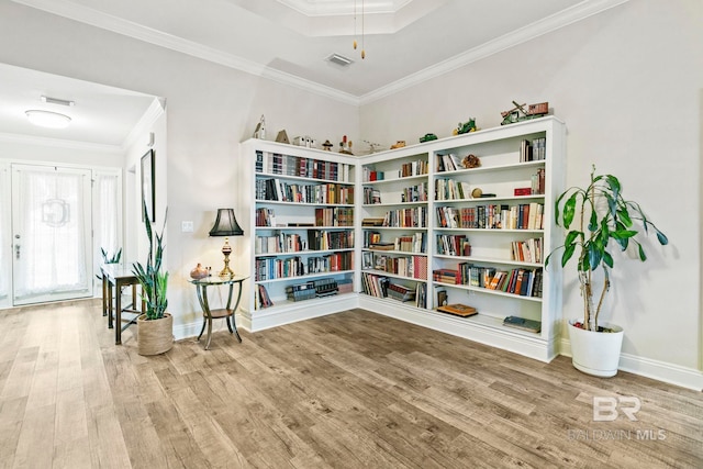 sitting room with a raised ceiling, wood-type flooring, and crown molding