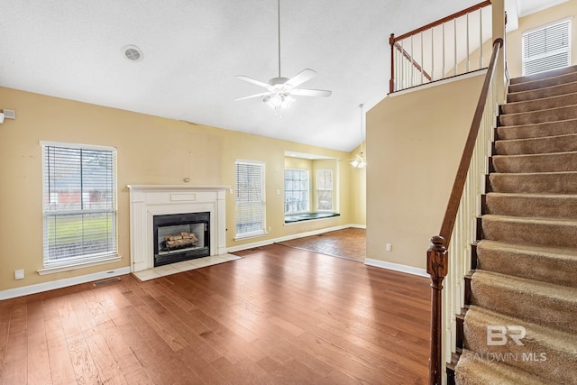 unfurnished living room featuring lofted ceiling, hardwood / wood-style flooring, a fireplace with flush hearth, baseboards, and stairs