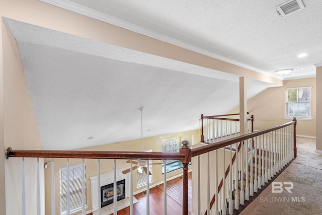 hallway with visible vents, lofted ceiling, wood finished floors, a textured ceiling, and an upstairs landing