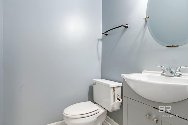 half bathroom with baseboards, vanity, and toilet