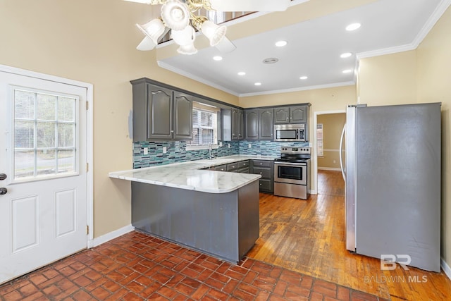 kitchen with baseboards, ornamental molding, a peninsula, gray cabinets, and stainless steel appliances