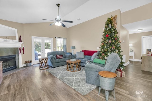 living room with ceiling fan, french doors, hardwood / wood-style floors, lofted ceiling, and a tiled fireplace