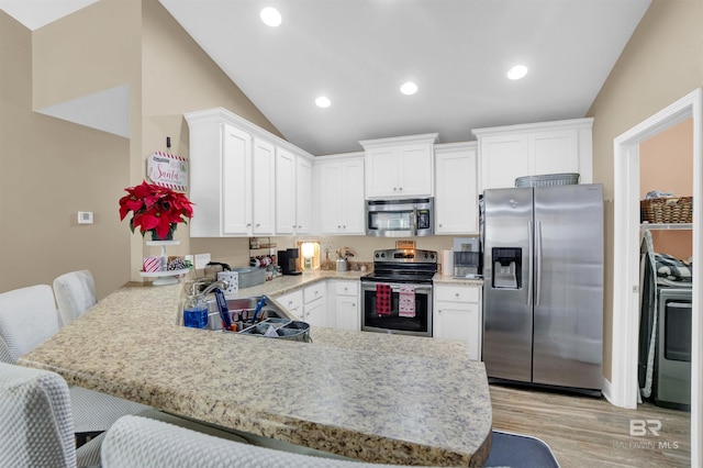 kitchen with kitchen peninsula, appliances with stainless steel finishes, a kitchen bar, light wood-type flooring, and white cabinetry