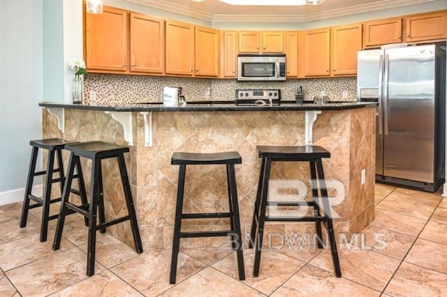 kitchen with crown molding, appliances with stainless steel finishes, kitchen peninsula, and a breakfast bar area