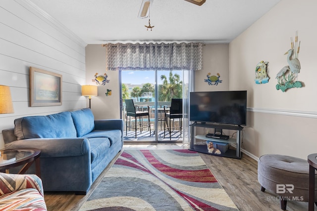 living room featuring ceiling fan, a textured ceiling, wood finished floors, baseboards, and ornamental molding