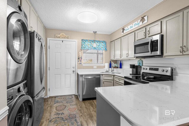 kitchen featuring stacked washing maching and dryer, sink, decorative light fixtures, light hardwood / wood-style flooring, and stainless steel appliances