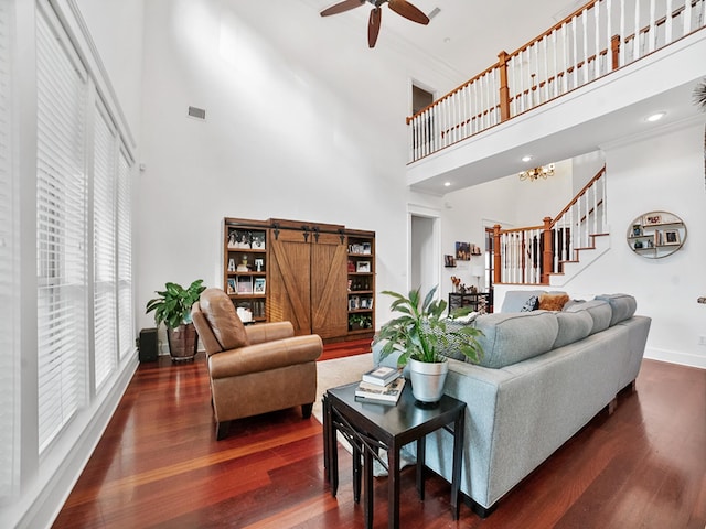 living room with ceiling fan with notable chandelier, a towering ceiling, dark hardwood / wood-style floors, and a barn door