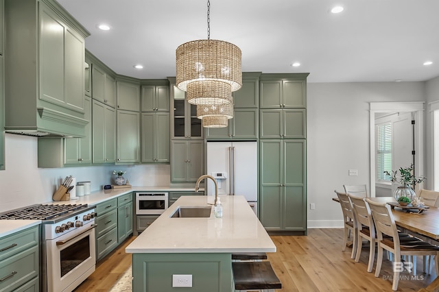 kitchen featuring sink, high quality appliances, light hardwood / wood-style floors, pendant lighting, and a kitchen island with sink