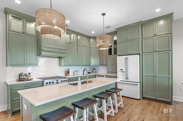 kitchen featuring sink, high end white refrigerator, light wood-type flooring, and decorative light fixtures