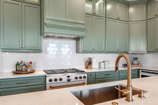 kitchen featuring oven, sink, green cabinets, high end stove, and decorative backsplash