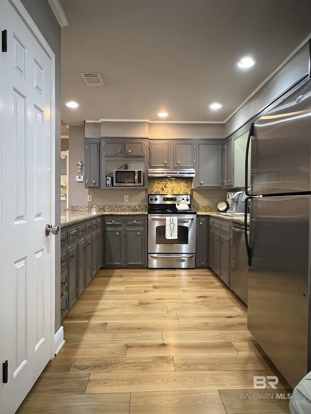 kitchen featuring gray cabinetry, light stone countertops, light hardwood / wood-style flooring, and stainless steel appliances