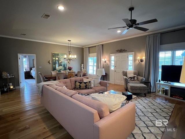 living room with ceiling fan with notable chandelier, wood-type flooring, and crown molding