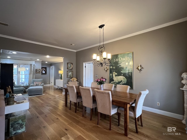 dining space with wood-type flooring, ornamental molding, and an inviting chandelier