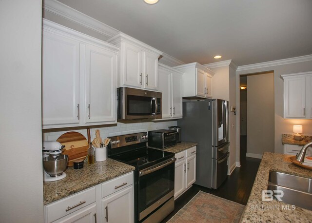 kitchen featuring backsplash, crown molding, appliances with stainless steel finishes, a sink, and white cabinetry