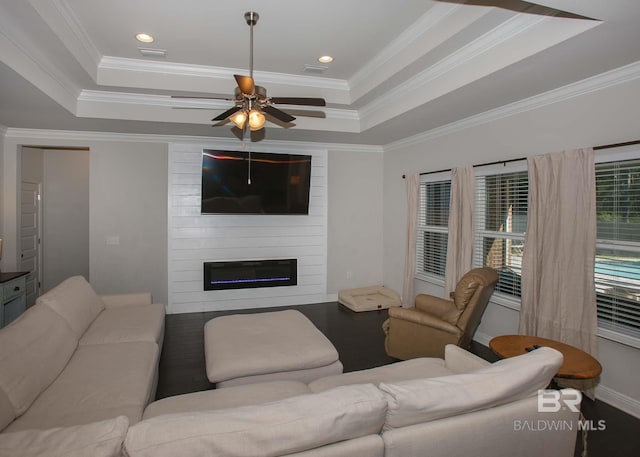 living room featuring a ceiling fan, crown molding, a large fireplace, a raised ceiling, and baseboards