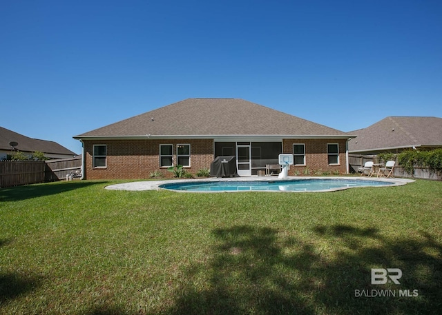 back of house featuring brick siding, a fenced backyard, a lawn, and a fenced in pool