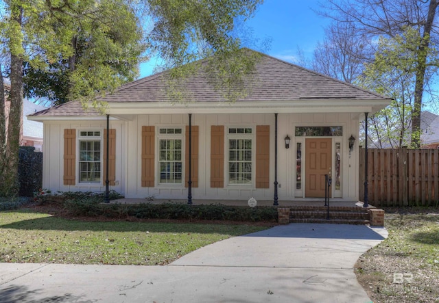 bungalow-style house with roof with shingles, covered porch, board and batten siding, fence, and a front lawn