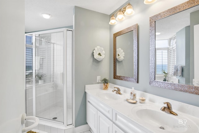 bathroom with double vanity, a stall shower, a textured ceiling, and a sink