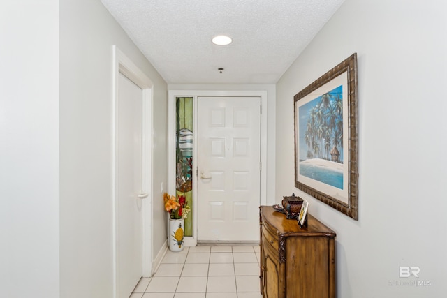 doorway to outside featuring a textured ceiling, baseboards, and light tile patterned floors