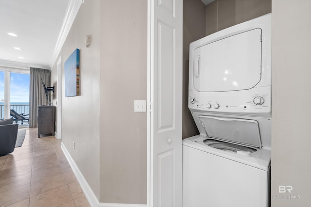 laundry room with stacked washer / dryer, baseboards, ornamental molding, light tile patterned floors, and laundry area