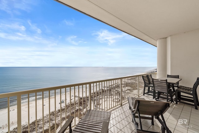 balcony with outdoor dining area, a view of the beach, and a water view