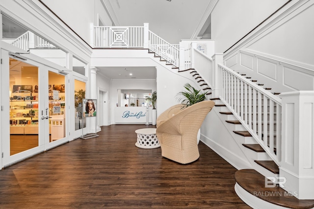 staircase with french doors, wood finished floors, a towering ceiling, and ornamental molding