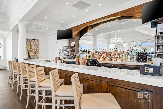 bar with wood finished floors, ornate columns, recessed lighting, ornamental molding, and a community bar