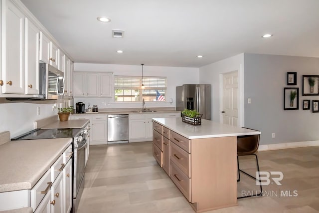kitchen featuring appliances with stainless steel finishes, light countertops, a kitchen island, a kitchen bar, and a sink