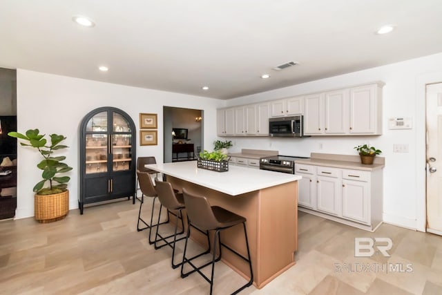 kitchen featuring a center island, a breakfast bar, visible vents, light countertops, and appliances with stainless steel finishes