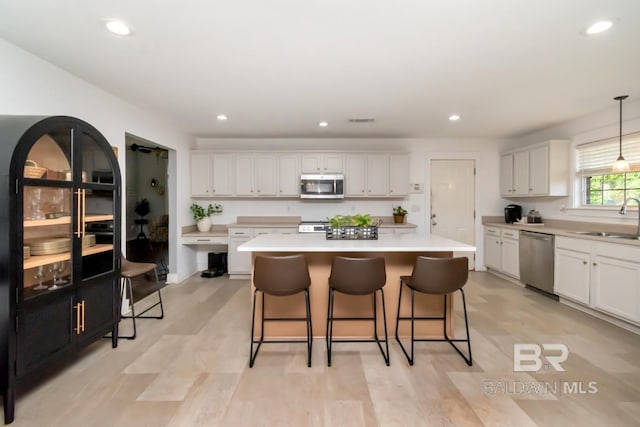 kitchen with a sink, a breakfast bar, a kitchen island, light countertops, and appliances with stainless steel finishes