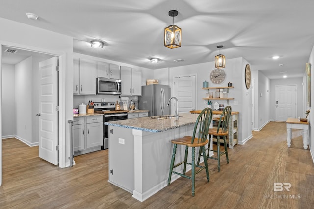 kitchen featuring a breakfast bar area, light stone counters, light hardwood / wood-style flooring, and stainless steel appliances