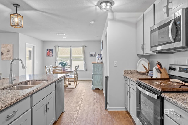 kitchen with appliances with stainless steel finishes, light wood-type flooring, light stone counters, sink, and pendant lighting