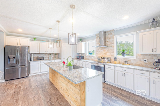 kitchen with an island with sink, sink, wall chimney exhaust hood, appliances with stainless steel finishes, and light hardwood / wood-style floors