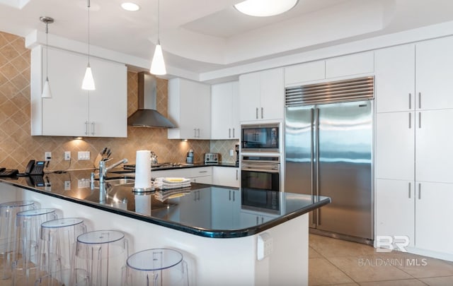 26302 Perdido Beach Blvd Unit D708, Orange Beach, AL 36561 - kitchen featuring built in appliances, wall chimney range hood, dark countertops, a peninsula, and a breakfast bar area