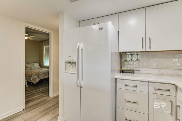 kitchen with white cabinetry, tasteful backsplash, light hardwood / wood-style flooring, white fridge with ice dispenser, and ceiling fan